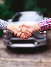 Apretón de manos frente a un carro, simbolizando la seguridad y el respaldo al comprar un vehículo en Usados Renting Colombia